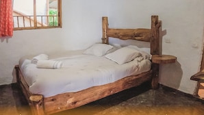 Un llit de fusta amb roba de llit blanca a una habitació amb una finestra i una cadira de fusta.