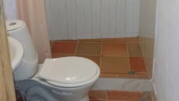 A small bathroom with a toilet, a shower area with tiled flooring, and a drain.