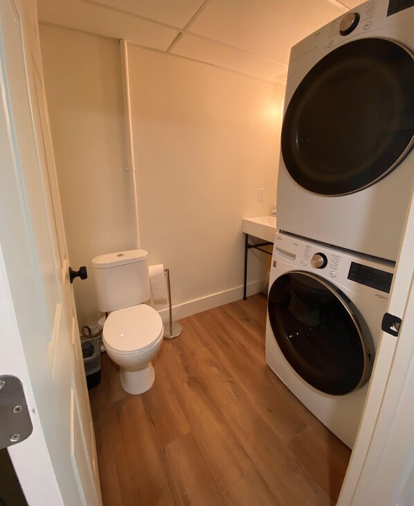 A compact bathroom with a toilet, a washing machine, and a small sink.