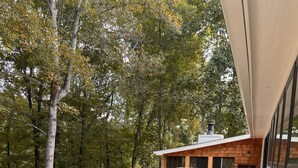 Una terraza de madera con una mesa, sillas, un banco y un edificio con amplios ventanales al fondo.