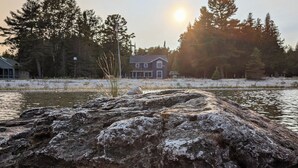 Et hus ved en sø med en klippefremspring foran og træer i baggrunden.