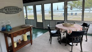 En hyggelig veranda med et skilt der siger 'Velkommen til vores veranda', et bord med stole og udsigt til stranden gennem store vinduer.