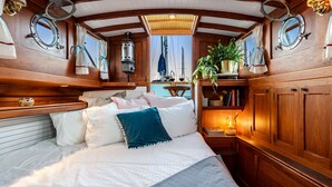 Une cabane chaleureuse avec un intérieur en bois, un lit avec une literie blanche et un coussin turquoise, une petite table avec une lampe et une plante en pot.