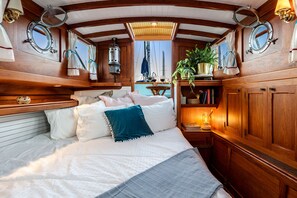 Una cabana acollidora amb interior de fusta, un llit amb roba de llit blanca i un coixí color aquamarina, una taula petita amb una làmpada, i una planta en test.