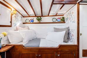 A cozy cabin interior with a wooden bed, a small table with a vase of flowers, and a ceiling with exposed beams.