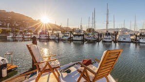 Un port de plaisance avec des bateaux amarrés, des chaises longues en bois et une vue dégagée sur le soleil se couchant sur l’eau.