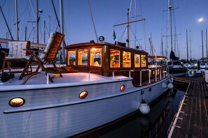 Een boot met een houten dek, een loungehoek met een comfortabele stoel, en een eethoek met tafels en stoelen.