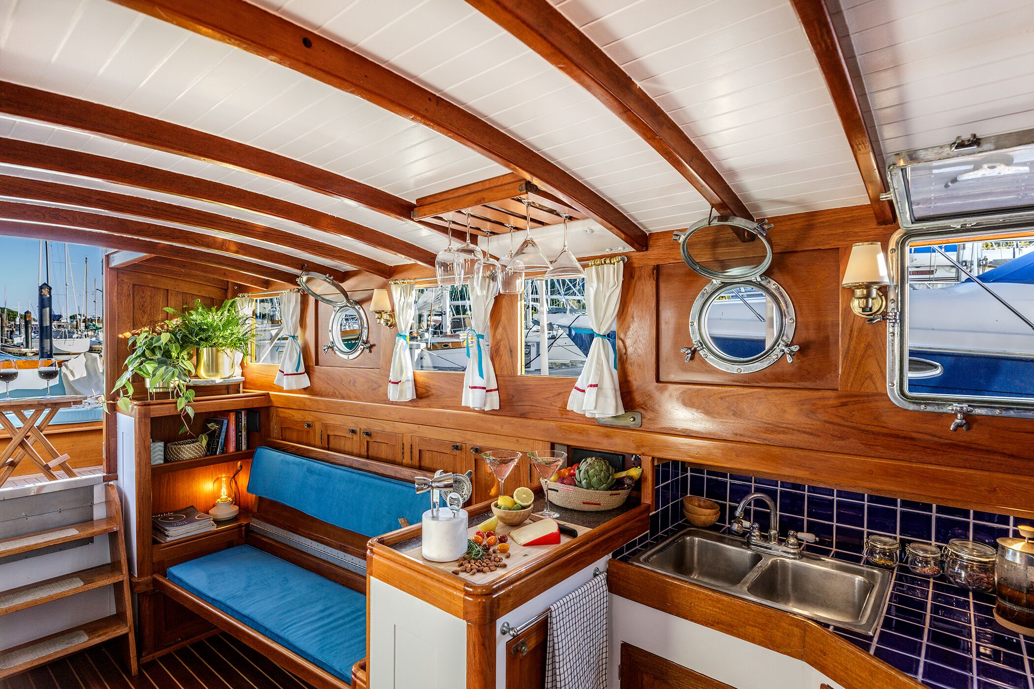 A compact galley with wooden cabinetry, a blue cushioned bench, a sink, and various food items.