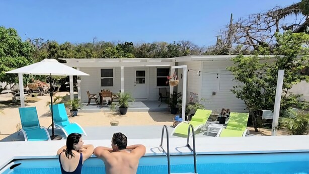 A swimming pool with lounge chairs and umbrellas, surrounded by a house and greenery. - Villa vanel (West End)