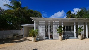 A white building with a covered porch, surrounded by palm trees and a clear blue sky. - Villa vanel (West End)
