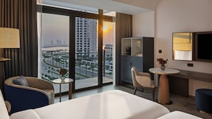 A hotel room with a large bed, a seating area with a table, a TV, and a view of a cityscape through a large window. -  Palace Dubai Creek Harbour (Dubai)