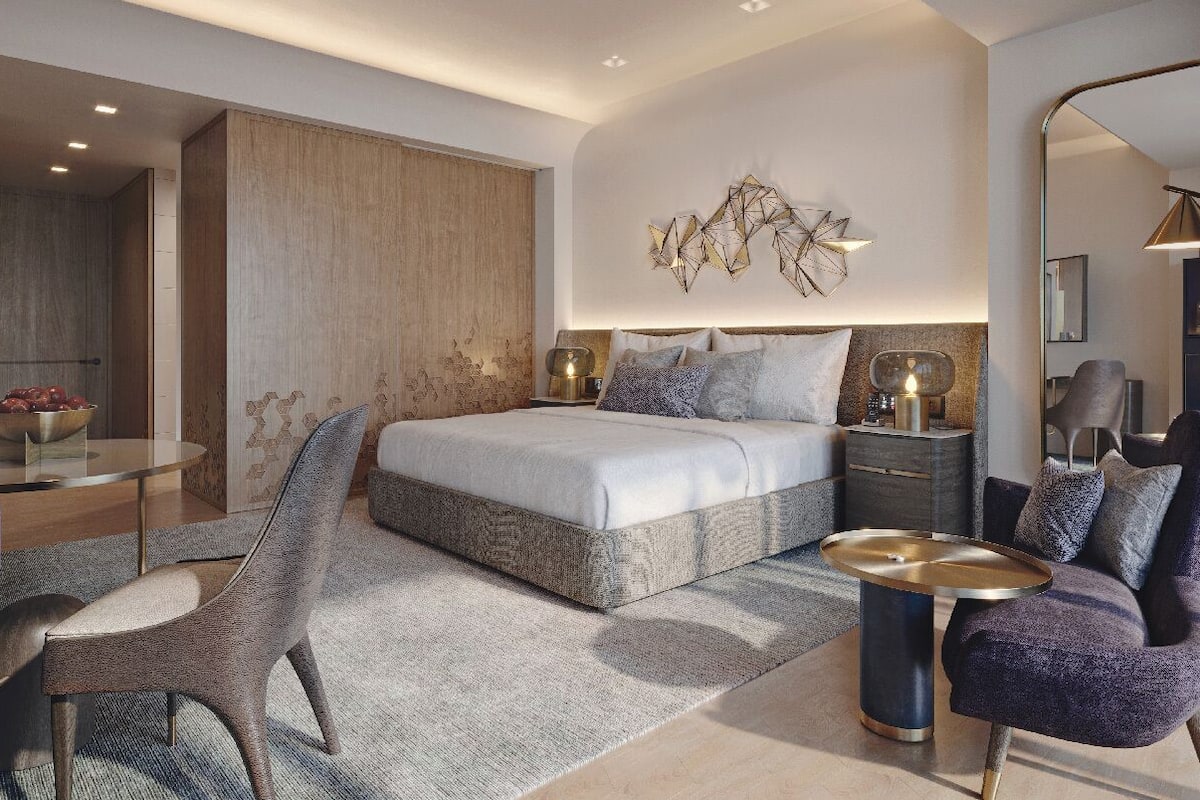 Een moderne slaapkamer met een bed, nachtkastjes, een stoel, een ronde tafel en een decoratief wandobject.