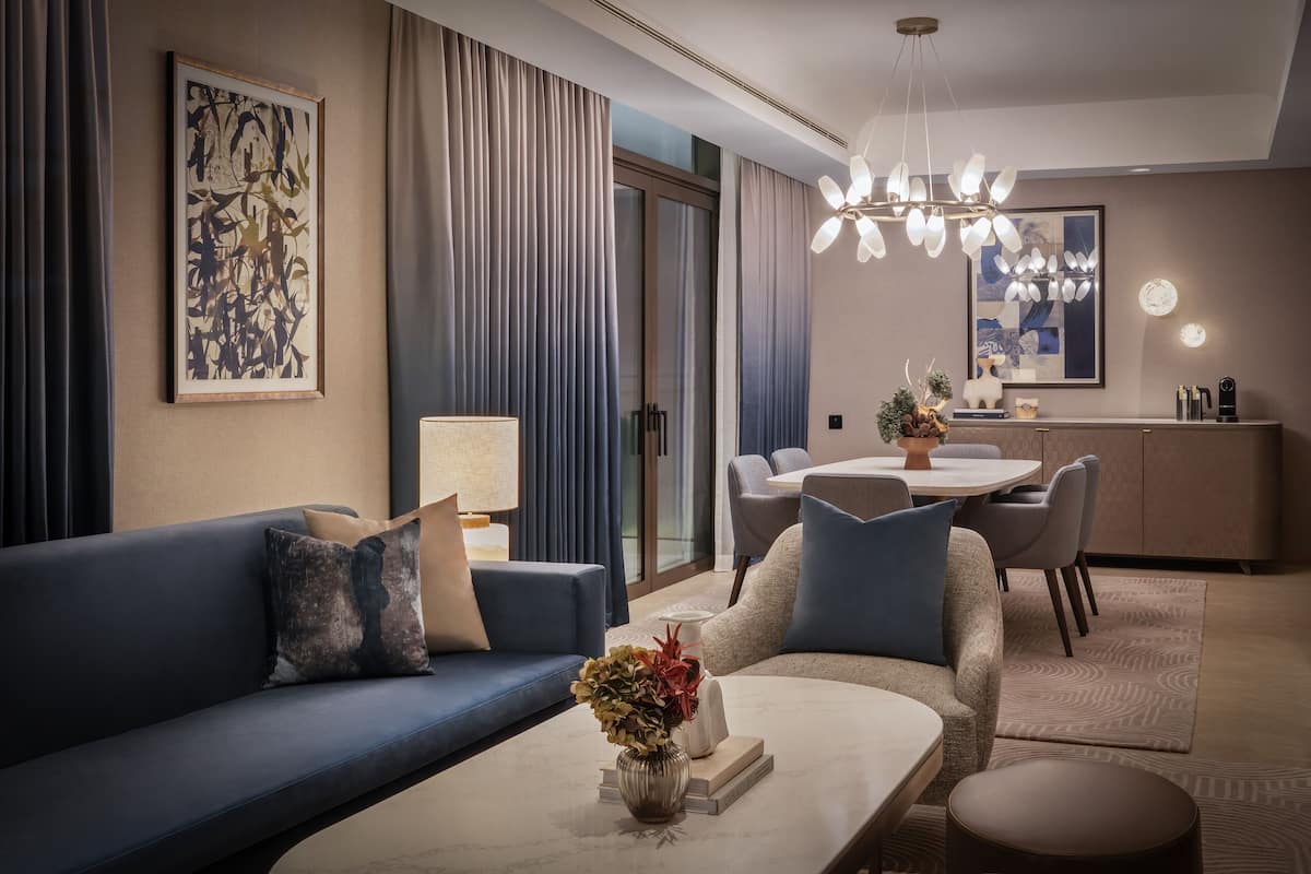 Een moderne hotelkamer met een bank, fauteuil, eettafel en een kroonluchter.