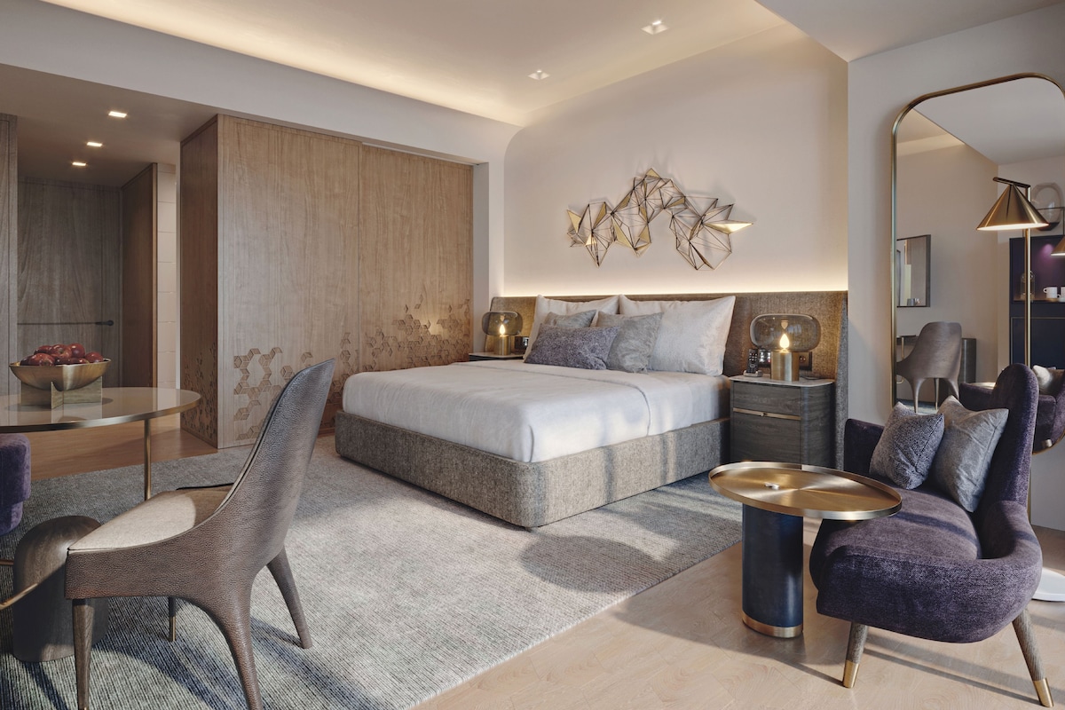Un dormitorio moderno con una cama grande, una mesita de noche, una silla y un espejo.