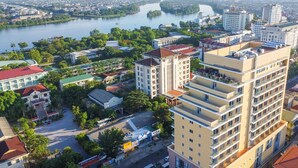 A multi-story hotel with a modern design, located near a river with a bridge in the background. - AD41 HOTEL HUE CS1 (Hue)