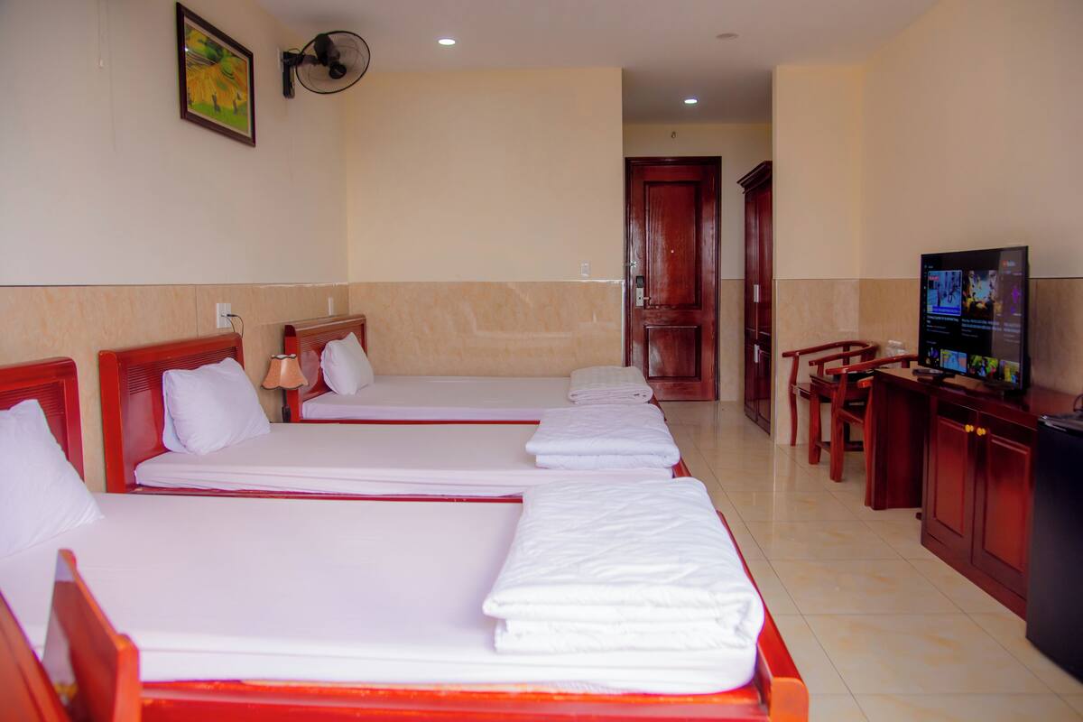 A hotel room with three beds, a television, and a desk with chairs.