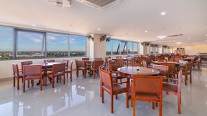 A spacious dining area with multiple round tables and chairs, large windows offering a city view, and ceiling fans. - AD41 HOTEL HUE CS1 (Hue)