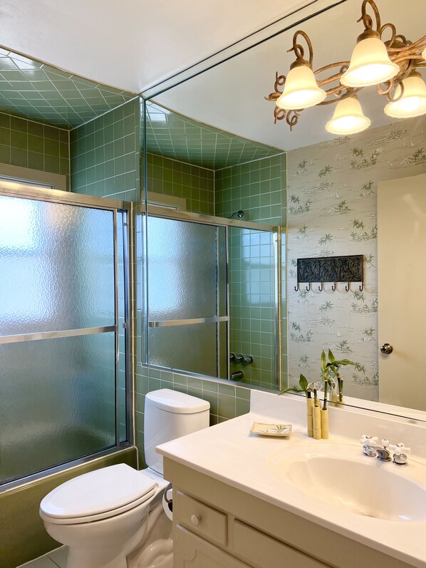 Un baño con ducha de vidrio, inodoro blanco, lavabo con espejo y lámpara de pared.