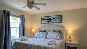 Una camera da letto con un letto, una ventola a soffitto, un comodino e una finestra con tende.