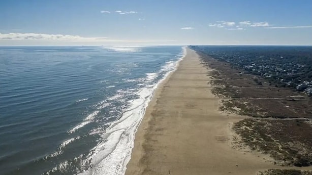 Vista aerea di una spiaggia con una lunga distesa di sabbia e una fila di case all'orizzonte.