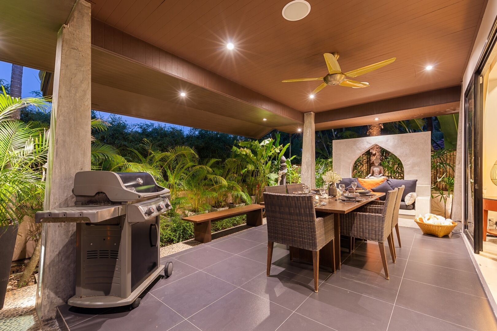 Une terrasse extérieure équipée d’un barbecue, d’une table à manger, de chaises et d’un ventilateur de plafond.
