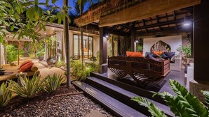 Un espace extérieur bien éclairé, doté d’un toit de chaume, entouré d ’une végétation luxuriante et de diverses plantes.