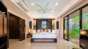 Une chambre spacieuse avec un grand lit, un ventilateur de plafond et une vue sur un jardin, visible à travers des portes vitrées.