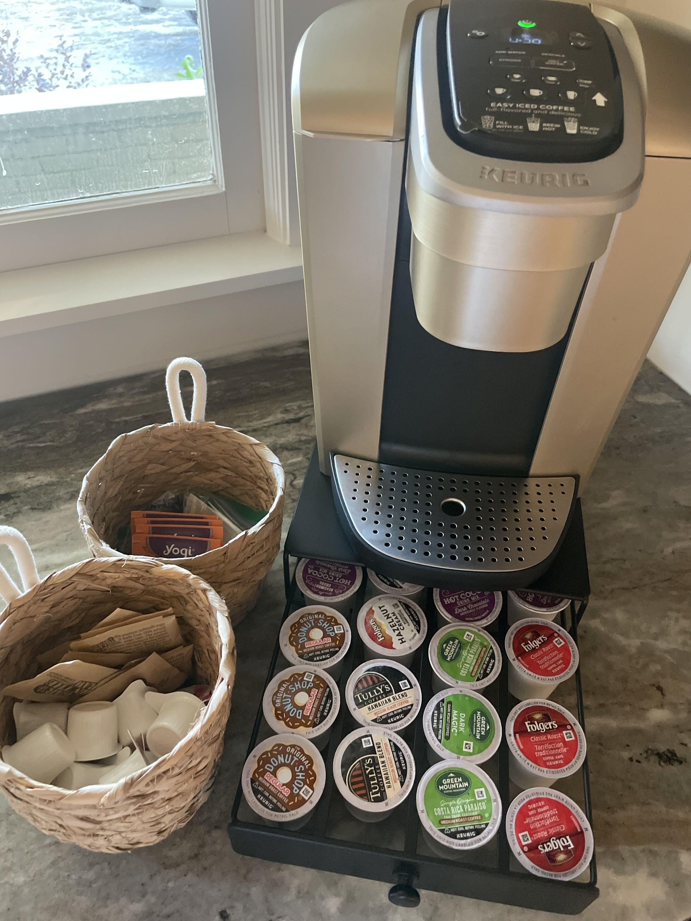 Eine Kaffeemaschine von Keurig, mit einer Auswahl an Kaffeekapseln und zwei Körben mit Kaffeebohnen.