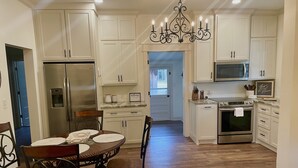 Una cocina moderna con armarios blancos, electrodomésticos de acero inoxidable y un comedor con mesa y sillas de madera.