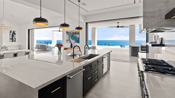 Una cocina moderna con una isla grande, luces colgantes y vistas al océano.