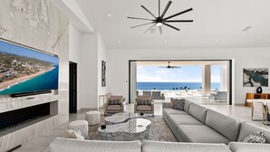 Una sala moderna con un televisor de pantalla plana grande, un sofá modular y vista a la playa a través del espacio abierto.