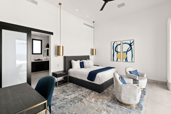 Una habitación de hotel moderna con una cama, dos sillones, un escritorio y un baño visible a través de una puerta abierta.