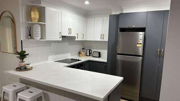 A modern kitchen with white cabinetry, a stainless steel refrigerator, a built-in oven, and a white countertop.