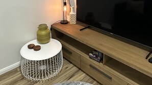 A modern living room with a large flat-screen TV, a round white side table with decorative items, a wooden entertainment unit, and a round white chair.