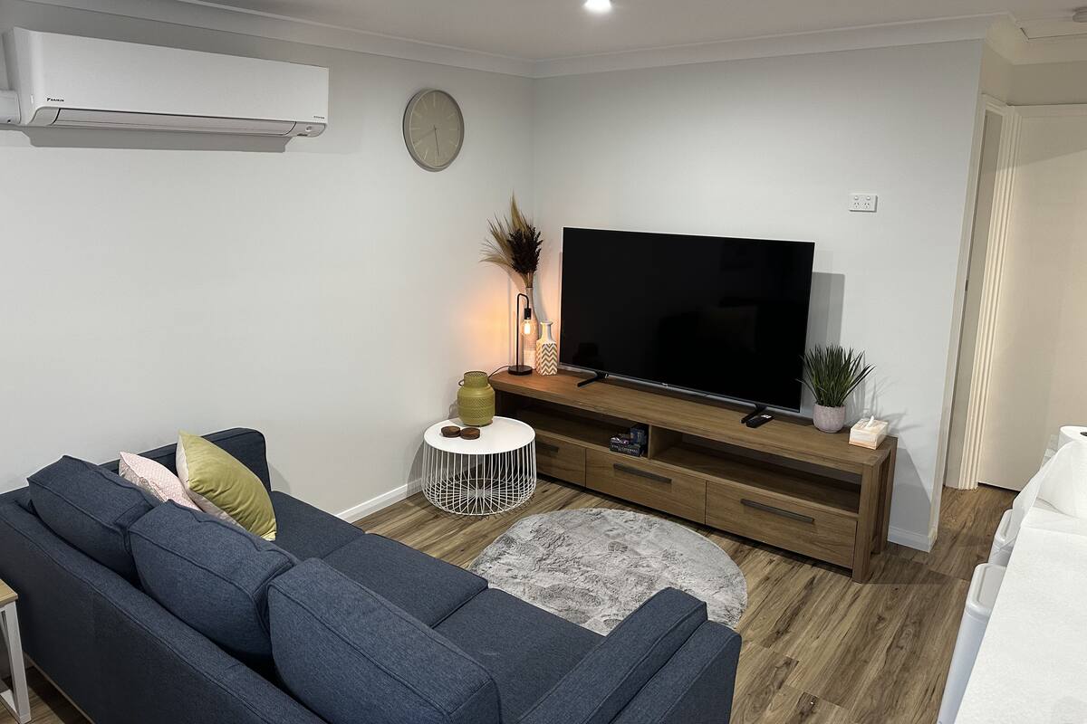 Un salon moderne doté d’un grand téléviseur à écran plat, d’un canapé gris foncé, d’une petite table basse ronde et d’un meuble TV en bois.