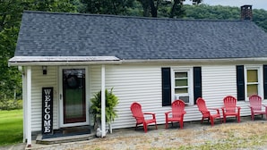 A white building with a dark roof, a 'WELCOME' sign, and four red chairs outside. - Ranch Style River Bungalow with Fireplace, River & 10 Acres at Houser's Crossing (Tamaqua)