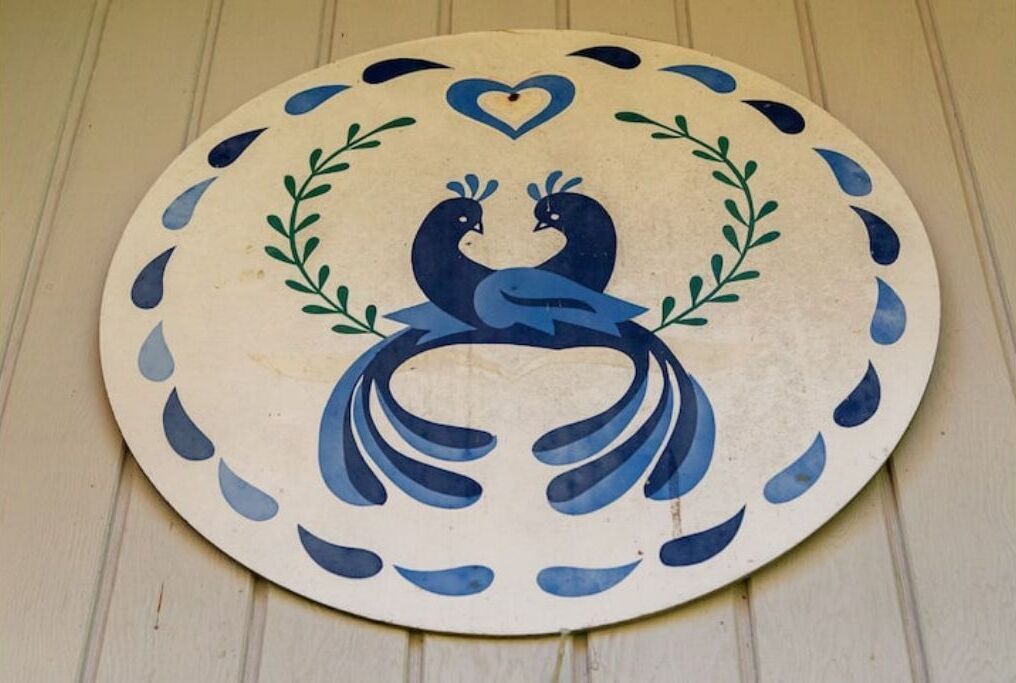 Objeto circular con diseño de pavo real, rodeado de formas de lágrima azules y un corazón en la parte superior.