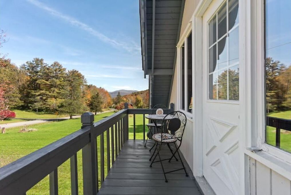 A covered porch with a table and chairs, overlooking a well-maintained lawn and trees.