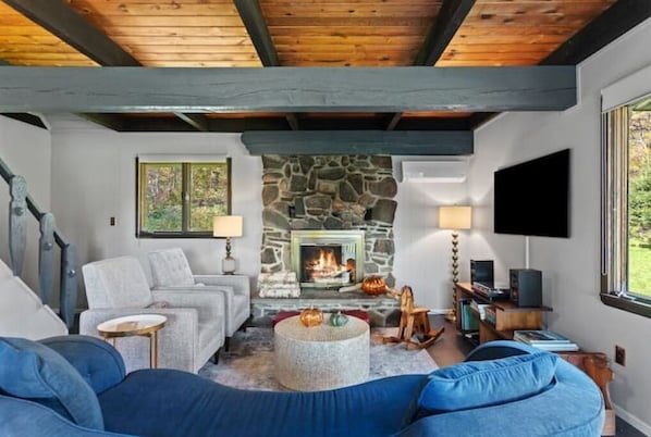 Uma sala de estar aconchegante com lareira de pedra, um sofá azul e uma televisão.