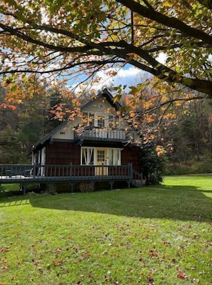 Uma cabana de madeira com varanda, rodeada por um gramado e árvores com folhas de outono.