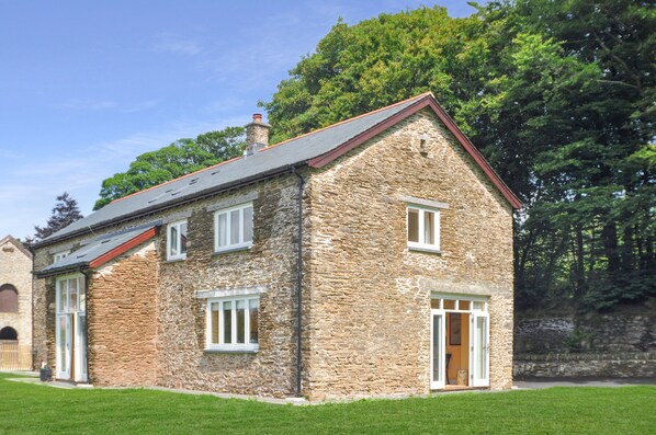 Une maison en pierre avec un toit en pente, de nombreuses fenêtres et une cheminée bien visible.