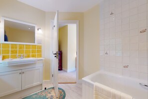 Une salle de bain avec un lavabo blanc, un miroir et une baignoire.