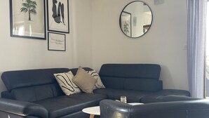 A modern living room with a dark blue sectional sofa, a round mirror, and framed artwork on the wall.
