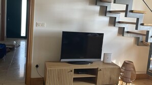 A modern living room with a built-in staircase, a flat-screen TV on a wooden console, and a decorative chair.