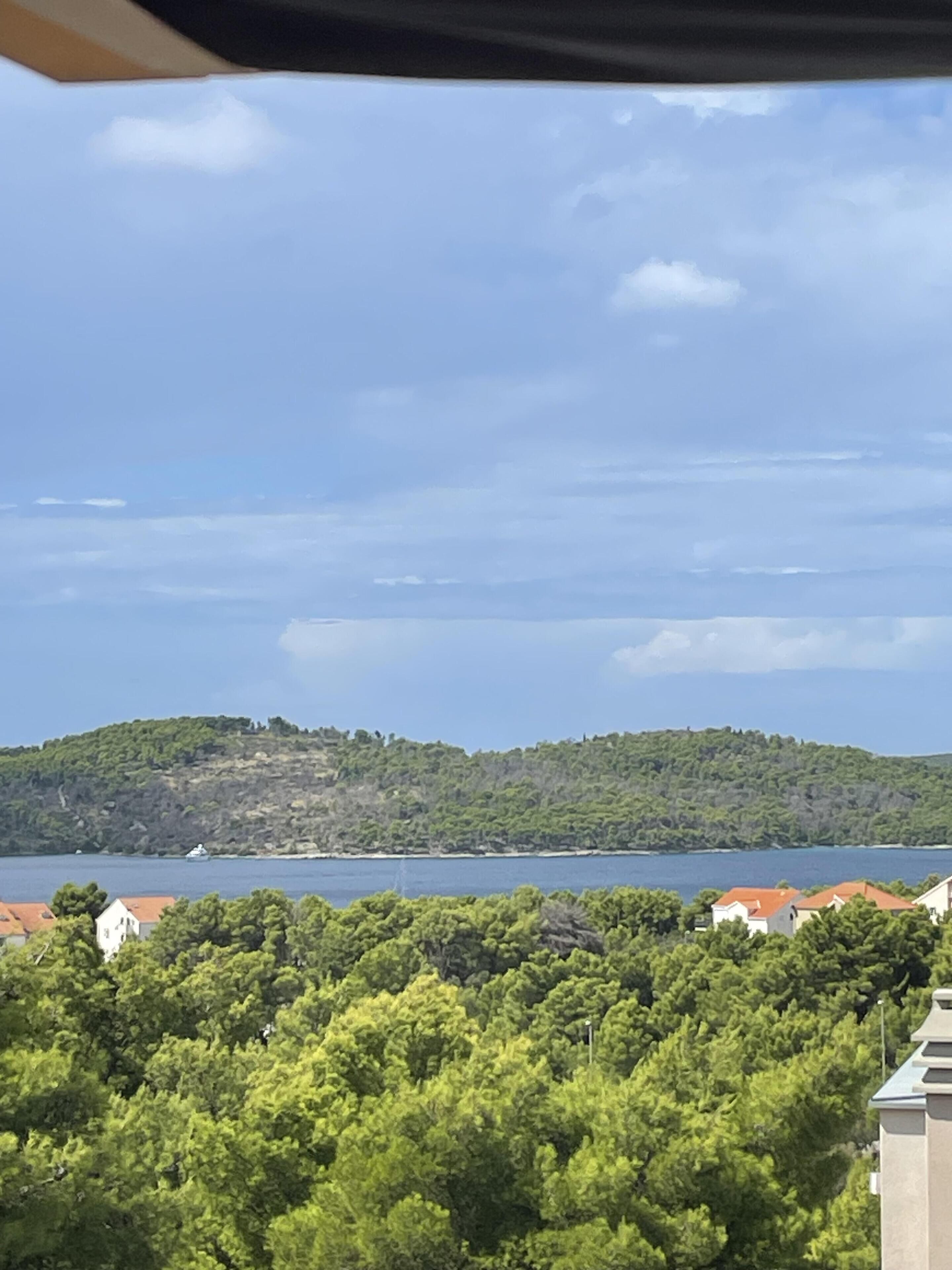 Ett kustlandskap med utsikt över en sjö, gröna kullar och byggnader med röda tak.