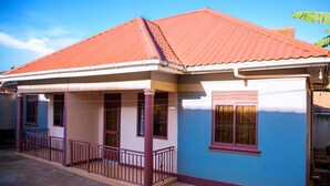A two-story house with a red roof, a balcony with a purple railing, and a window with a purple frame. - Beautiful 2-Bed house in Kampala (Kampala)