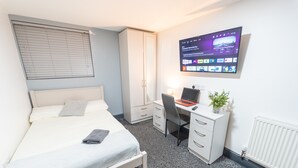 Un dormitorio con cama, escritorio y televisor montado en la pared.