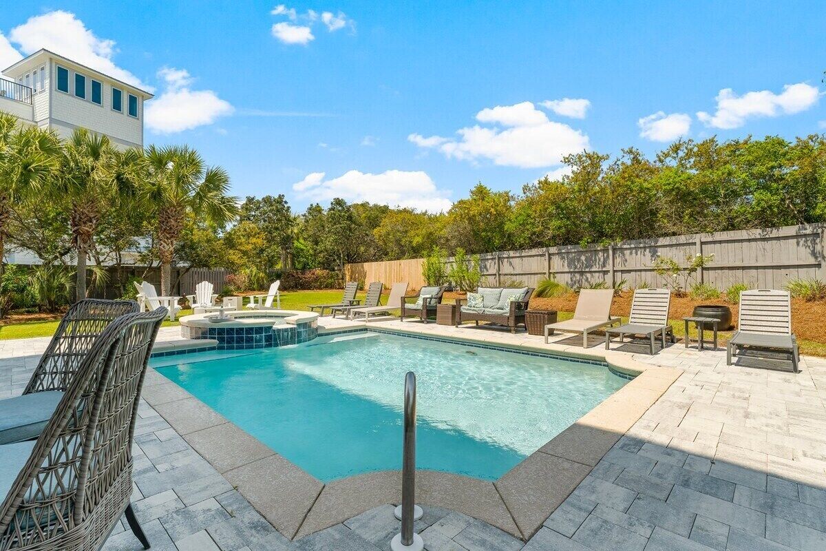 Una piscina rectangular con solárium empedrado, rodeada de sillones de descanso y una valla de madera.