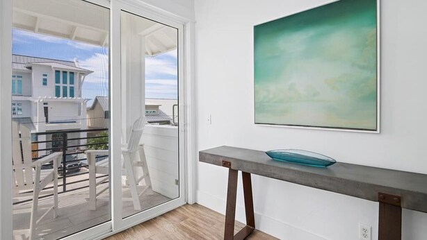 Un interno moderno con una porta scorrevole in vetro che dà su un balcone, un tavolino minimalista con una ciotola di vetro e un grande quadro astratto appeso al muro.