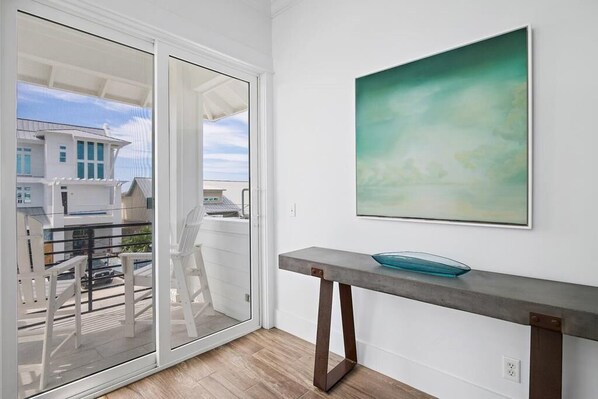 A modern interior with a sliding glass door leading to a balcony, a minimalist table with a glass bowl, and a large abstract painting on the wall.